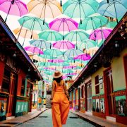 Woman walking on a Colombian street under an art installation made of colorful umbrellas.