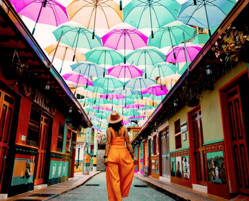 Woman walking on a Colombian street under an art installation made of colorful umbrellas.