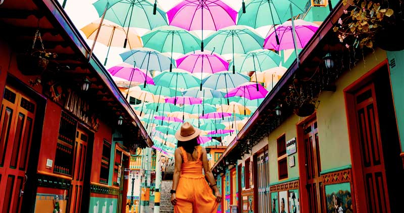 Woman walking on a Colombian street under an art installation made of colorful umbrellas.